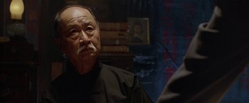 Movie still from “The Replacement Killers” (1998), directed by Antoine Fuqua – An older man in a black shirt is looking into the distance; Close Up shot, Over the shoulder angle