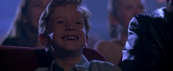 Movie still from “The Replacement Killers” (1998), directed by Antoine Fuqua – A young boy smiling while sitting in a chair; Close Up shot, Low angle