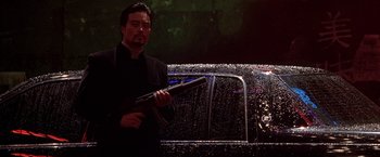 Movie still from “The Replacement Killers” (1998), directed by Antoine Fuqua – A man holding a gun while standing in front of a car; Medium shot, Low angle
