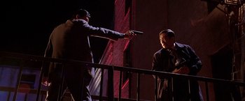 Movie still from “The Replacement Killers” (1998), directed by Antoine Fuqua – A man pointing a gun at another man in a black suit; Medium shot, Low angle