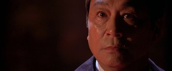 Movie still from “The Replacement Killers” (1998), directed by Antoine Fuqua – An older man looking at the camera in a dark room; Close Up shot, Low angle