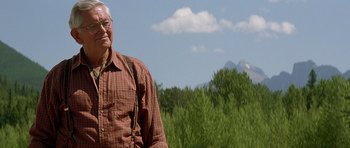 Movie still from “The River Wild” (1994), directed by Curtis Hanson – An older man standing in front of some trees and mountains; Medium shot, Low angle