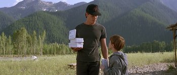 Movie still from “The River Wild” (1994), directed by Curtis Hanson – A man and a boy are standing in a field with boxes; Medium shot, Over the shoulder angle
