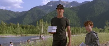 Movie still from “The River Wild” (1994), directed by Curtis Hanson – A man holding a stack of pizza boxes in his hands; Medium shot, Low angle