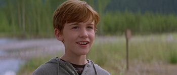 Movie still from “The River Wild” (1994), directed by Curtis Hanson – A young boy with red hair smiling for the camera; Close Up shot, Over the shoulder angle