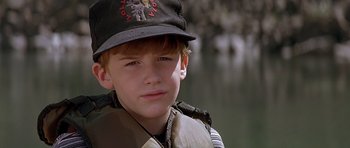 Movie still from “The River Wild” (1994), directed by Curtis Hanson – A young boy wearing a baseball cap and vest; Close Up shot, High angle