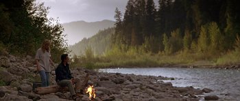 Movie still from “The River Wild” (1994), directed by Curtis Hanson – A man sitting on a rock near a fire; Wide shot, Low angle