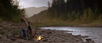 Movie still from “The River Wild” (1994), directed by Curtis Hanson – A man sitting on the rocks near a fire; Extreme Wide shot, Over the shoulder angle