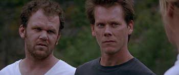 Movie still from “The River Wild” (1994), directed by Curtis Hanson – Two men standing next to each other in front of trees; Close Up shot, Low angle