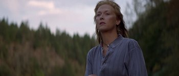 Movie still from “The River Wild” (1994), directed by Curtis Hanson – A woman standing in front of a forest looking to her left; Close Up shot, Low angle