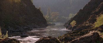 Movie still from “The River Wild” (1994), directed by Curtis Hanson – A river flowing through a lush green forest; Extreme Wide shot, High angle