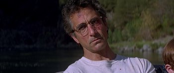 Movie still from “The River Wild” (1994), directed by Curtis Hanson – A person wearing glasses and a white t shirt; Close Up shot, Low angle