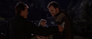 Movie still from “The River Wild” (1994), directed by Curtis Hanson – A man holding another man's hand while standing in the dark; Medium shot, Over the shoulder angle