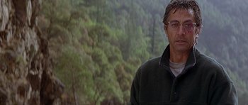 Movie still from “The River Wild” (1994), directed by Curtis Hanson – A person wearing a jacket near a forest; Close Up shot, Over the shoulder angle