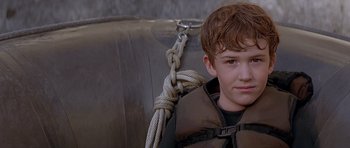 Movie still from “The River Wild” (1994), directed by Curtis Hanson – A young boy sitting in a boat with a rope tied to it; Close Up shot, Over the shoulder angle