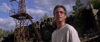 Movie still from “The River Wild” (1994), directed by Curtis Hanson – A man with glasses standing in front of some rocks; Close Up shot, Low angle