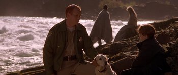 Movie still from “The River Wild” (1994), directed by Curtis Hanson – A man and a dog are on the beach; Medium shot, Over the shoulder angle
