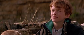 Movie still from “The River Wild” (1994), directed by Curtis Hanson – A young man is smiling for the camera outside; Close Up shot, Low angle
