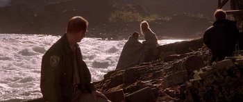 Movie still from “The River Wild” (1994), directed by Curtis Hanson – A man and a woman sitting on a rock near a body of water; Wide shot, Over the shoulder angle