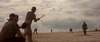 Movie still from “The Rookie” (2002), directed by John Lee Hancock – A group of men playing a game of baseball on the beach; Wide shot, Over the shoulder angle