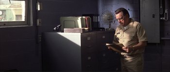 Movie still from “The Rookie” (2002), directed by John Lee Hancock – A man in uniform looking at papers in front of a filing cabinet; Medium shot, Low angle