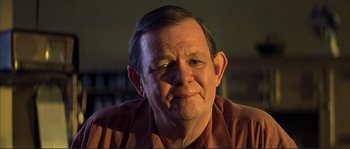 Movie still from “The Rookie” (2002), directed by John Lee Hancock – An older man wearing a brown shirt with a smirk on his face; Close Up shot, Low angle