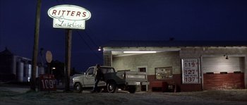 Movie still from “The Rookie” (2002), directed by John Lee Hancock – A man standing in front of a truck at a gas station at night; Wide shot, Low angle