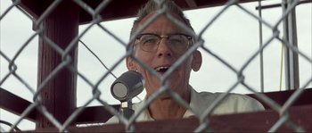 Movie still from “The Rookie” (2002), directed by John Lee Hancock – An older man with glasses is holding a microphone; Close Up shot, Low angle