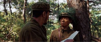 Movie still from “The Sacrifice” (2020), directed by Yang Lu – Two men in military uniforms talking to each other in the woods; Medium shot, Over the shoulder angle