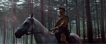 Movie still from “The Sacrifice” (2020), directed by Yang Lu – A man riding on the back of a white horse through the woods; Medium shot, Low angle