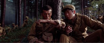 Movie still from “The Sacrifice” (2020), directed by Yang Lu – Two young men sitting next to each other near a tree; Medium shot, Low angle