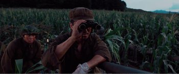 Movie still from “The Sacrifice” (2020), directed by Yang Lu – A man looking through a pair of binoculars in a corn field; Medium shot, Low angle