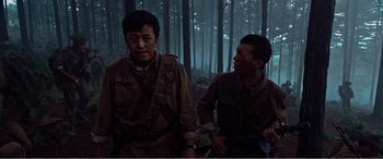 Movie still from “The Sacrifice” (2020), directed by Yang Lu – A couple of men standing next to each other in the woods; Medium shot, Low angle