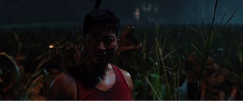 Movie still from “The Sacrifice” (2020), directed by Yang Lu – A man in a red tank top is in a field; Close Up shot, Over the shoulder angle