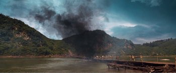 Movie still from “The Sacrifice” (2020), directed by Yang Lu – Smoke billows from a mountain near a body of water; Extreme Wide shot, High angle
