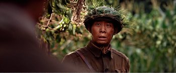 Movie still from “The Sacrifice” (2020), directed by Yang Lu – A man wearing a hat with grass on top of his head; Close Up shot, Over the shoulder angle