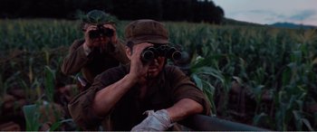 Movie still from “The Sacrifice” (2020), directed by Yang Lu – A man in a field looking through binoculars; Medium shot, Low angle