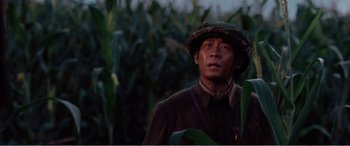 Movie still from “The Sacrifice” (2020), directed by Yang Lu – A man standing in a corn field wearing a hat; Close Up shot, Low angle