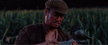 Movie still from “The Sacrifice” (2020), directed by Yang Lu – A man wearing a brown hat is looking at a piece of paper; Close Up shot, Low angle