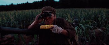 Movie still from “The Sacrifice” (2020), directed by Yang Lu – A man holding a cob of corn while looking through binoculars; Medium shot, Low angle