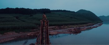 Movie still from “The Sacrifice” (2020), directed by Yang Lu – A man standing on top of a wooden bridge over a river; Extreme Wide shot, High angle