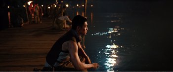 Movie still from “The Sacrifice” (2020), directed by Yang Lu – A man sitting on a dock looking out at a body of water at night; Medium shot, Over the shoulder angle