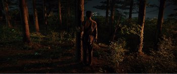 Movie still from “The Sacrifice” (2020), directed by Yang Lu – A man standing next to a tree in the woods at night; Wide shot, High angle