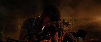 Movie still from “The Sacrifice” (2020), directed by Yang Lu – A man with blood all over his face smoking a cigarette in front of a crowd; Close Up shot, High angle