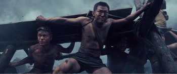 Movie still from “The Sacrifice” (2020), directed by Yang Lu – A shirtless man holding a wooden board on top of a boat; Medium shot, Low angle