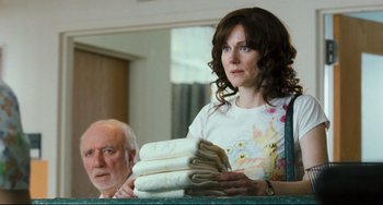 Movie still from “The Savages” (2007), directed by Tamara Jenkins – A woman holding a stack of folded towels next to an older man; Medium shot, Over the shoulder angle