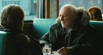Movie still from “The Savages” (2007), directed by Tamara Jenkins – An older man sitting at a table with a glass of water in front of him; Medium shot, Over the shoulder angle