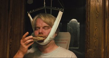 Movie still from “The Savages” (2007), directed by Tamara Jenkins – A man wearing a neck brace eating a sandwich; Medium shot, Overhead angle