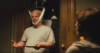 Movie still from “The Savages” (2007), directed by Tamara Jenkins – A man wearing a neck brace while holding a plate in his mouth; Medium shot, Over the shoulder angle