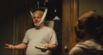 Movie still from “The Savages” (2007), directed by Tamara Jenkins – A man wearing a neck brace while standing in a room; Medium shot, Over the shoulder angle